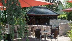 Un patio al aire libre con suelo de ladrillo, sillas de mimbre y mesas bajo sombrillas naranjas.