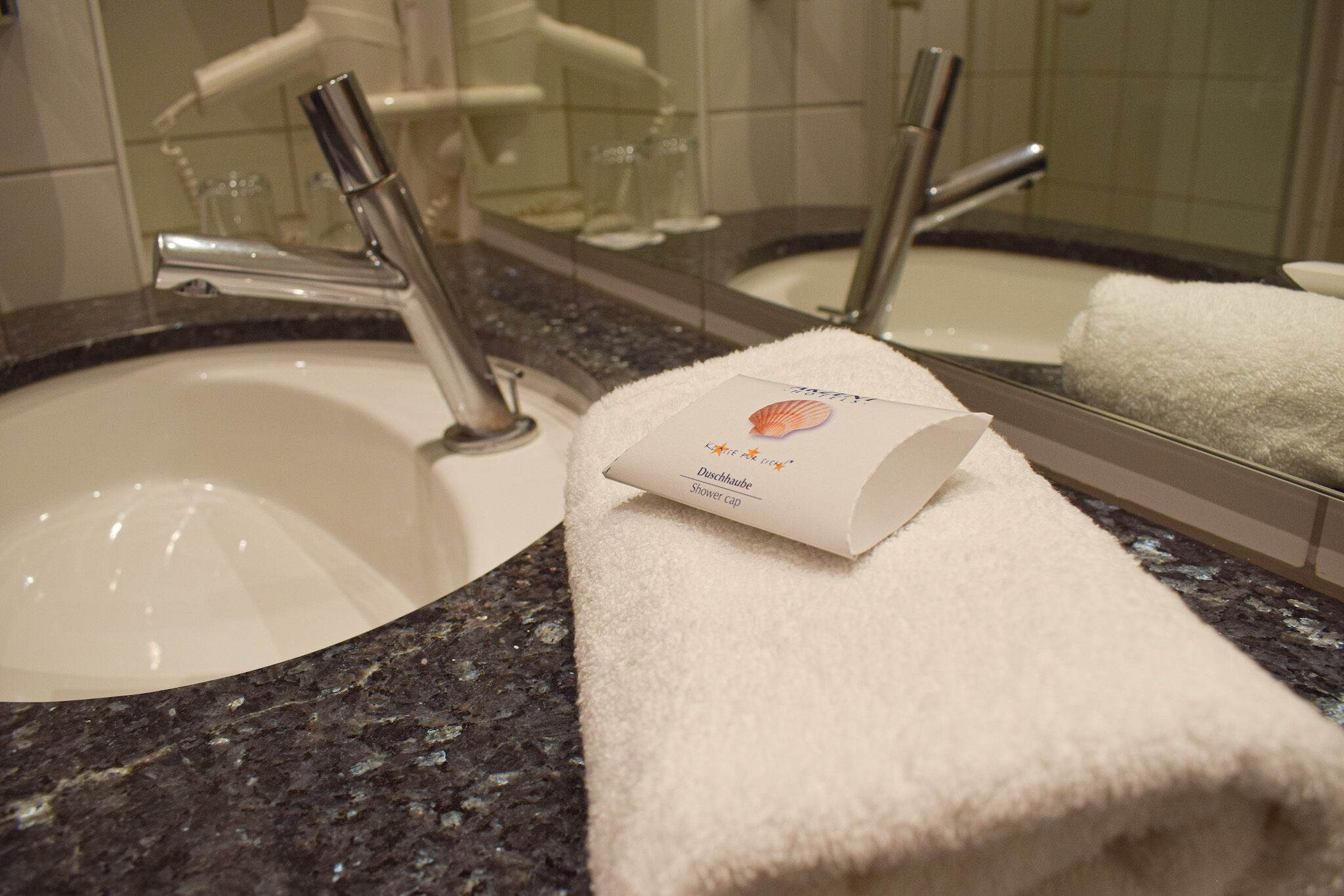 A bathroom with a sink, mirror, and a towel with a shower cap.