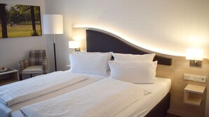 Habitación de hotel con una cama grande, dos mesitas de noche, una silla y una lámpara de pared.