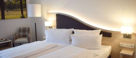Habitación de hotel con una cama grande, dos mesitas de noche, una silla y una lámpara de pared.