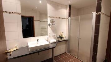 A modern bathroom with a large mirror, a sink, and a shower area.