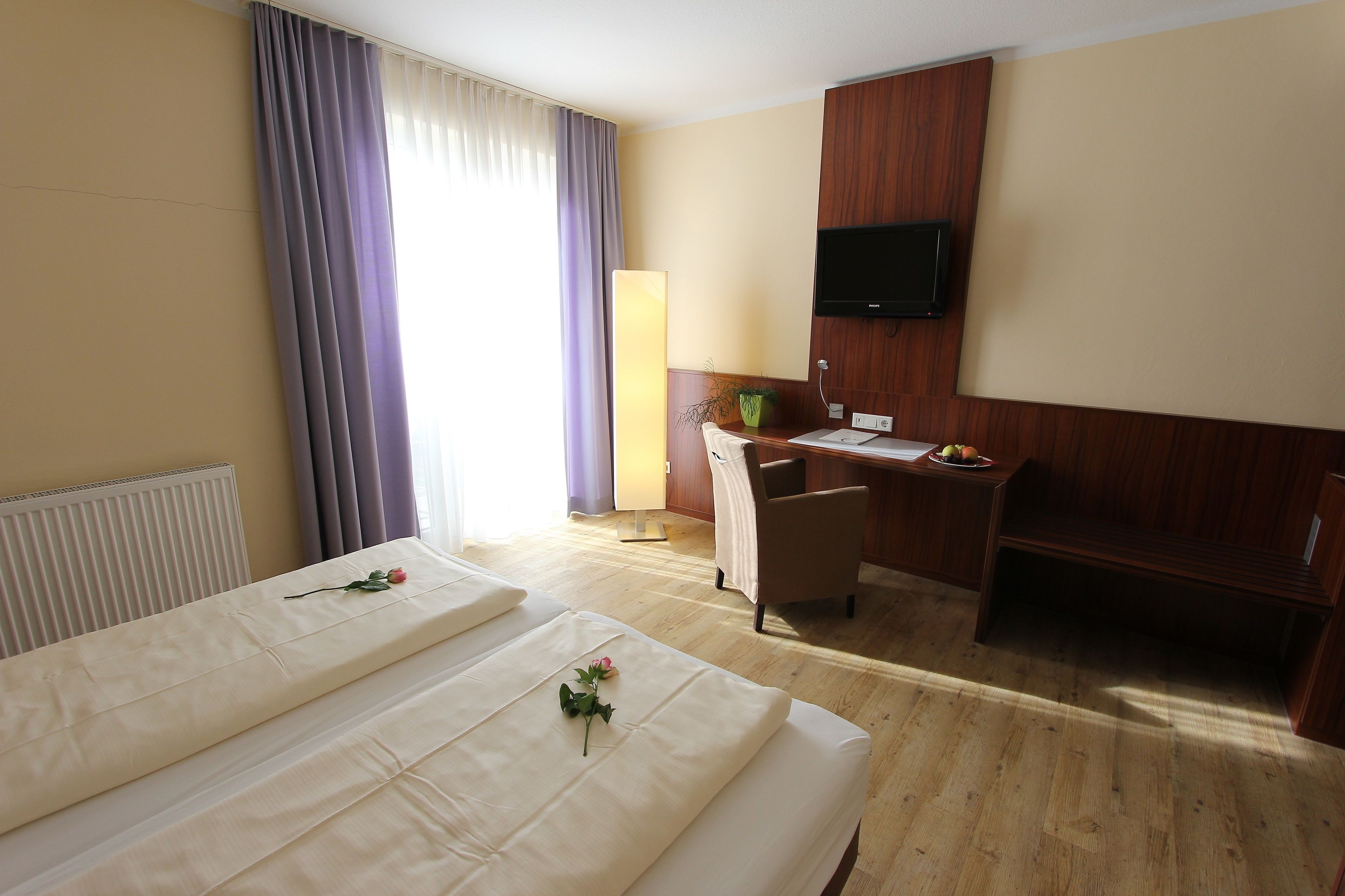 A hotel room with two beds, a desk, a chair, a TV, and a window with curtains.