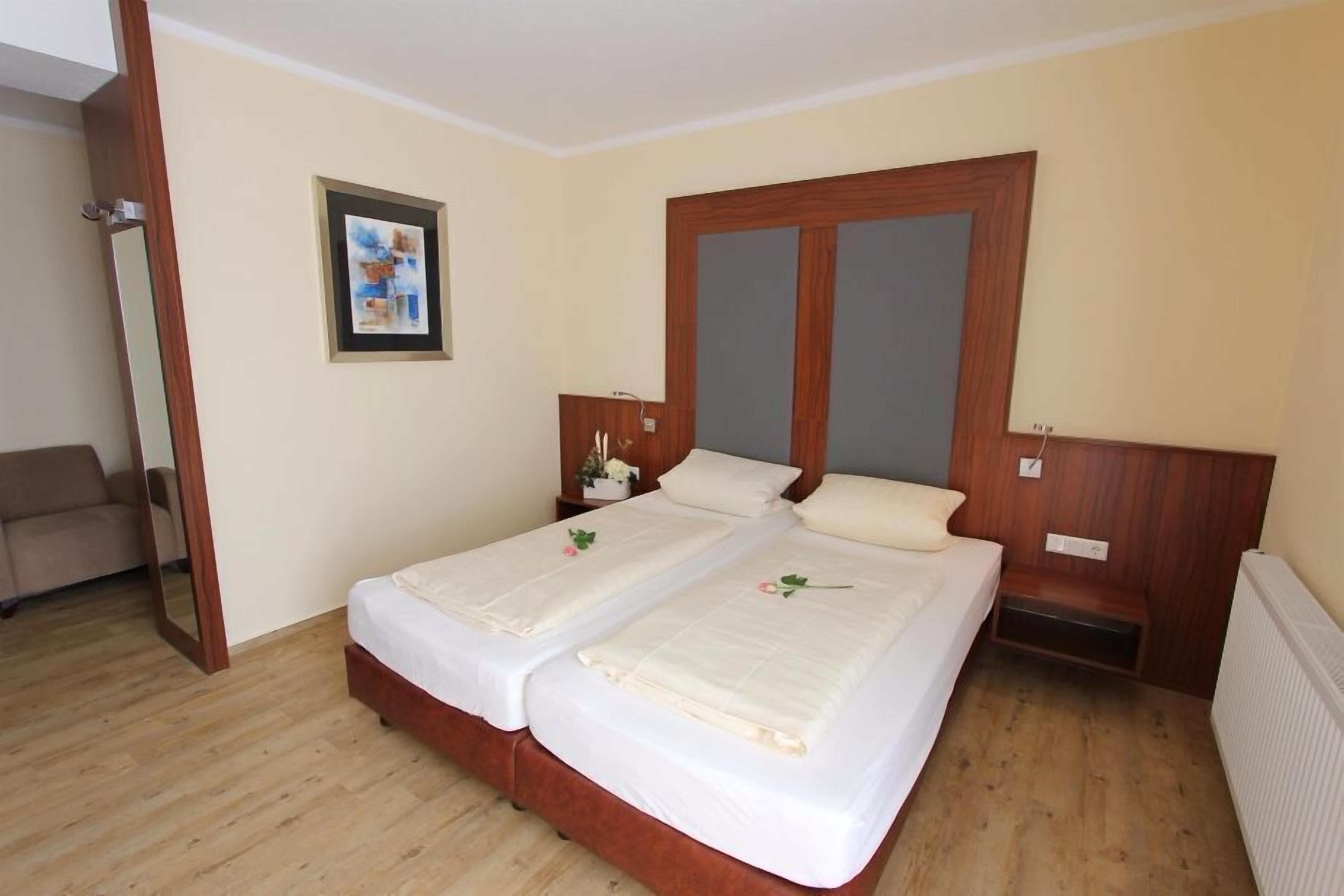 Una cama doble con cabecera de madera, una mesita de noche con lámpara y un cuadro en la pared.