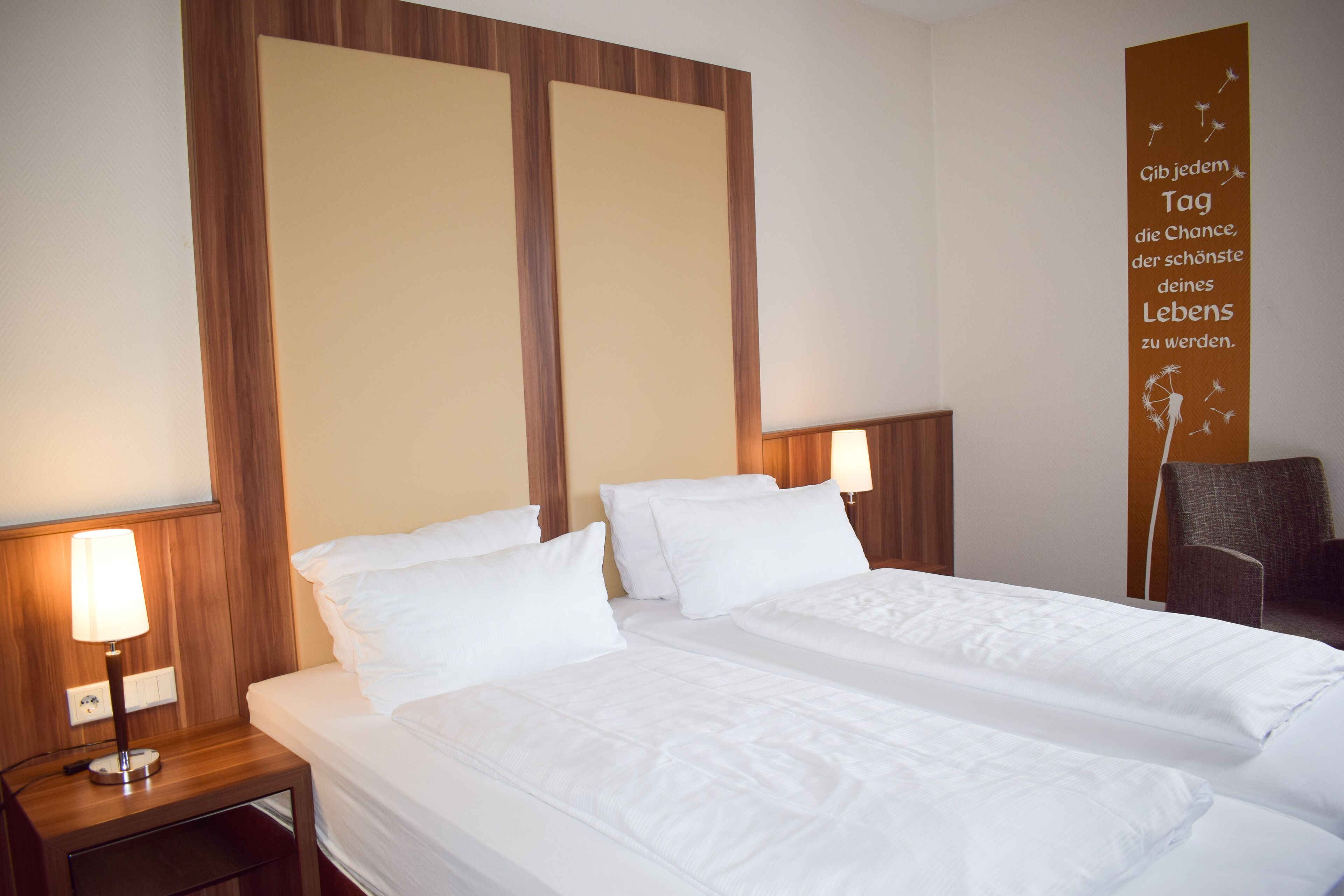 Quarto de hotel com duas camas e cabeceiras de madeira, além de uma parede com uma frase motivacional.