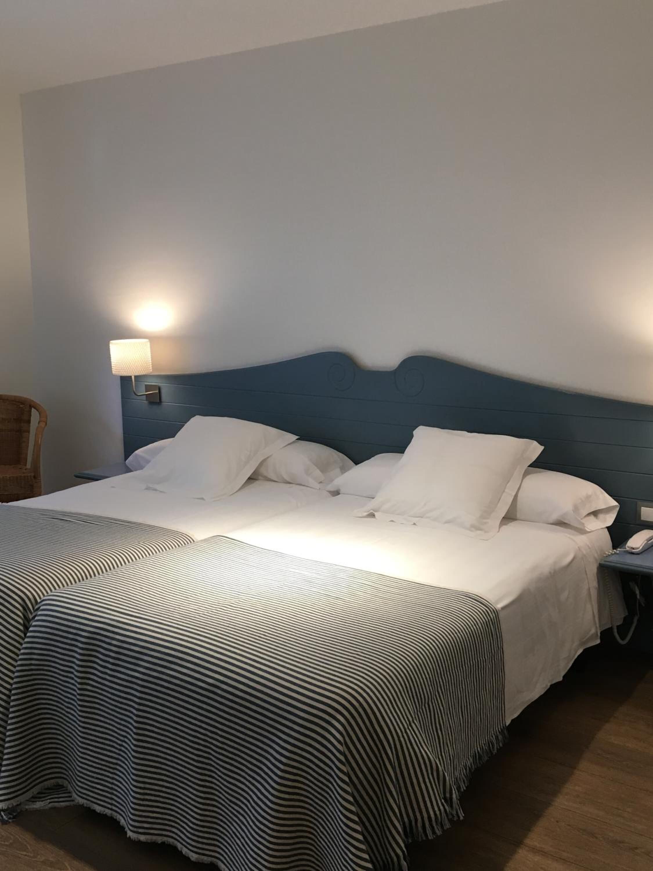 Una cama doble con cubrecama a rayas, cabecera, lámpara de noche y teléfono en la mesita.