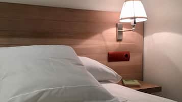Ein Hotelzimmer mit einem hölzernen Kopfteil, einer Nachttischlampe, einem Nachttisch mit einem roten Gegenstand und einem grünen Buch.