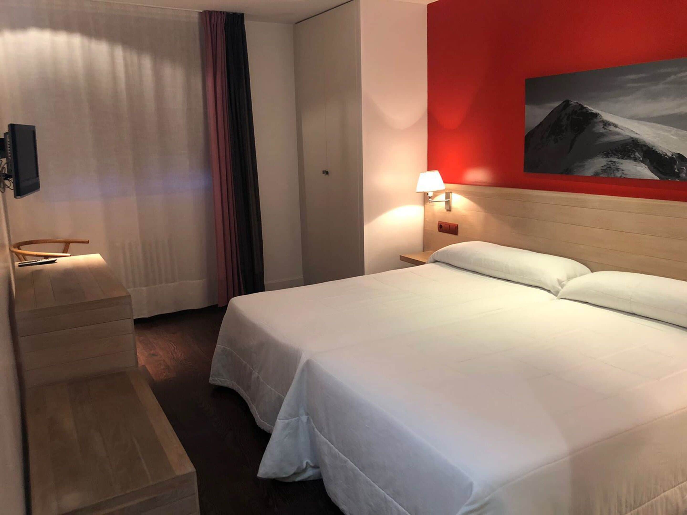 A hotel room with a bed, a nightstand with a lamp, a painting on the wall, and a curtain.