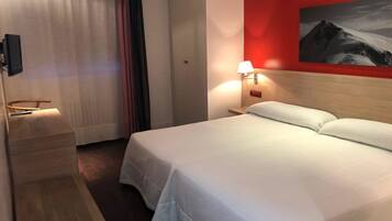 A hotel room with a bed, a nightstand with a lamp, a painting on the wall, and a curtain.