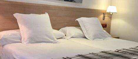 A neatly made bed with white linens and a plaid throw blanket, a wooden headboard, and a wall-mounted lamp.