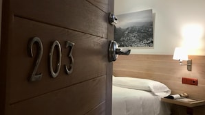 A hotel room with a wooden door marked '203', a bed, a nightstand with a lamp, and a wall-mounted picture.