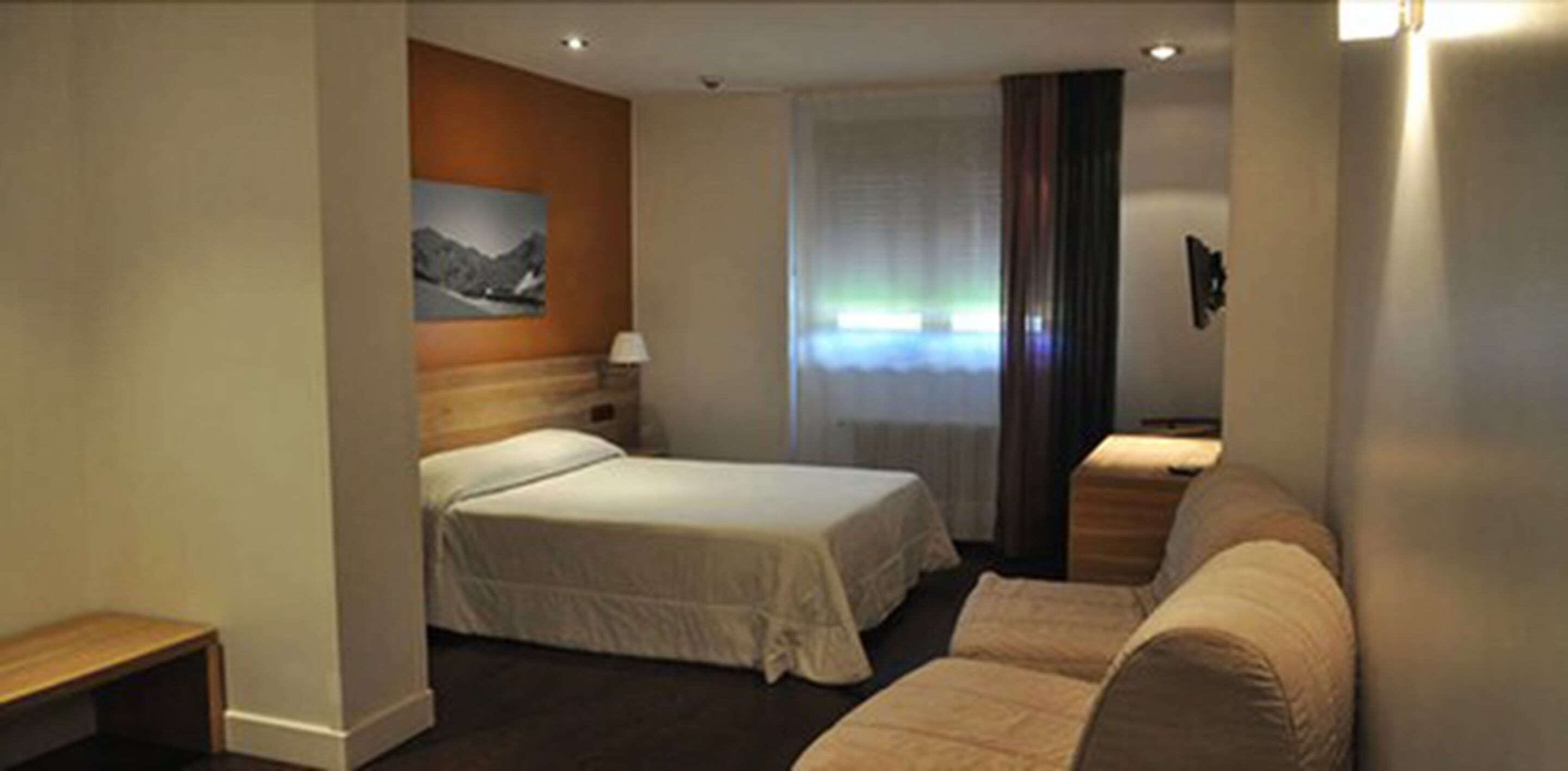 A hotel room with two beds, a sofa, a painting on the wall, and a window with curtains.