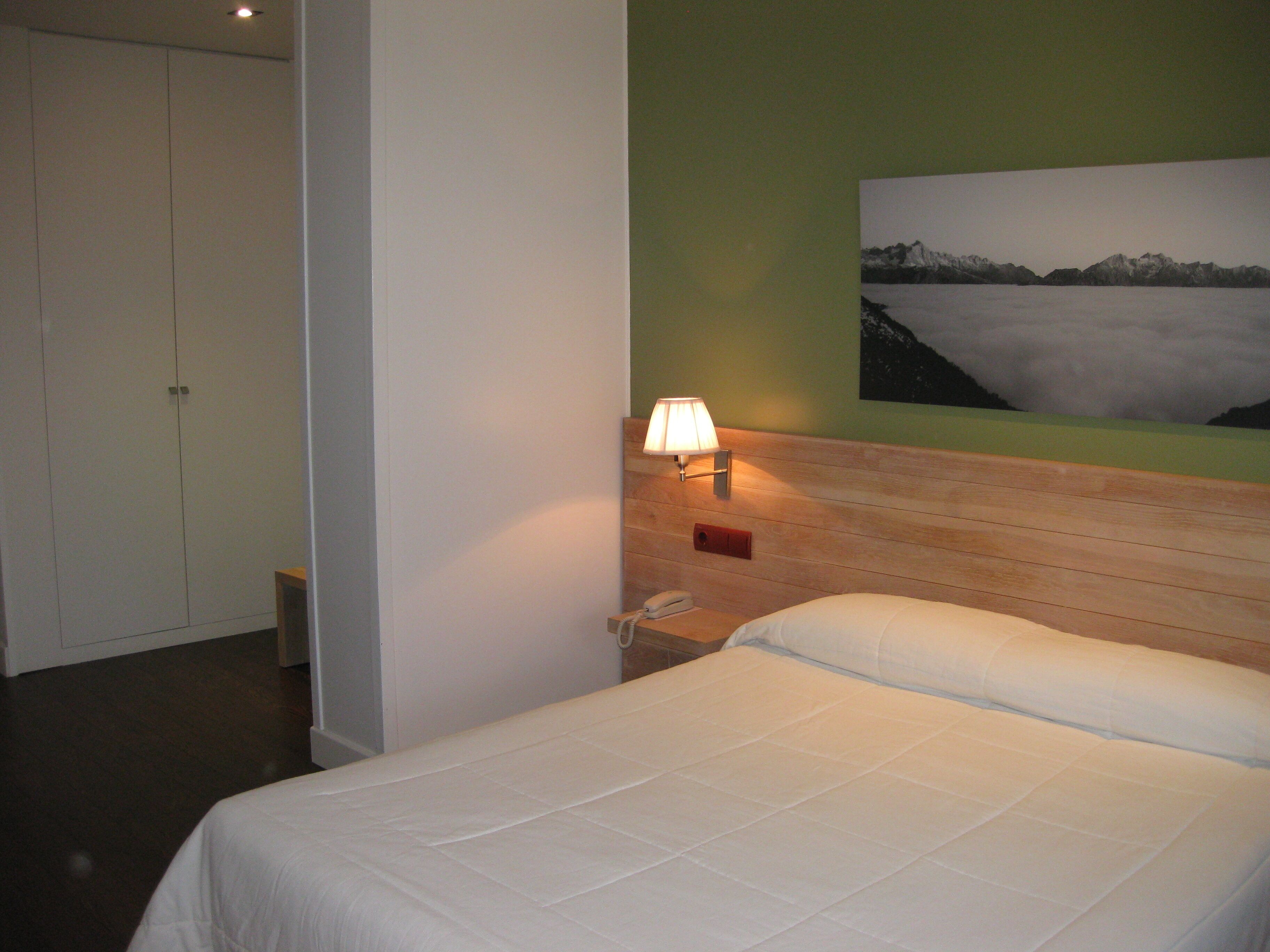Una habitación de hotel con cama, mesita de noche, lámpara y un cuadro en la pared.