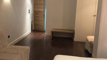 A hotel room with a bed, a chair, a bench, and a wardrobe.