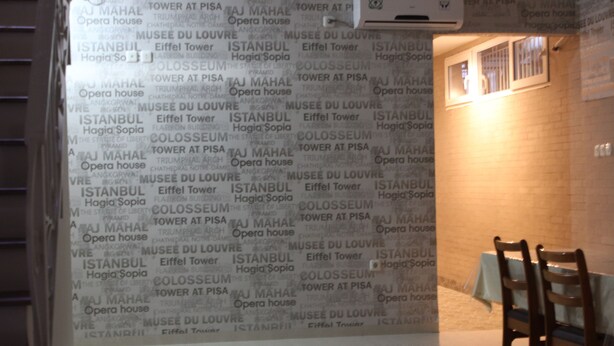 A room with a wall covered in text, a table with a white tablecloth, and two wooden chairs. - Permata Inn (Medan)