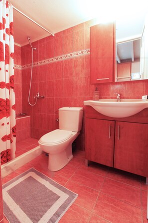 A bathroom with a shower, toilet, sink, and cabinets.