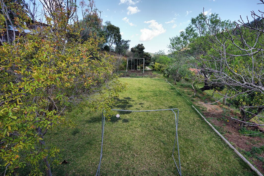 Un patio trasero con césped, un columpio metálico y una manguera de jardín.