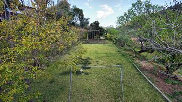 Un patio trasero con césped, un columpio metálico y una manguera de jardín.