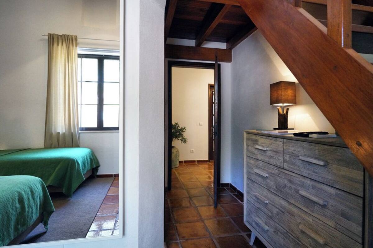 A bedroom with two beds, a wooden dresser, and a lamp.