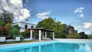 A swimming pool with a covered seating area, a white building with a chimney, and lush greenery in the background. - Vale Fuzeiros Nature Guest House (Silves)