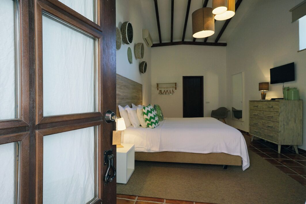 A bedroom with a bed, bedside table, lamp, and a dresser.