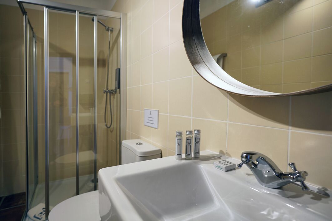 Un baño con cabina de ducha de vidrio, un lavamanos blanco con grifo cromado y un espejo redondo sobre el lavamanos.