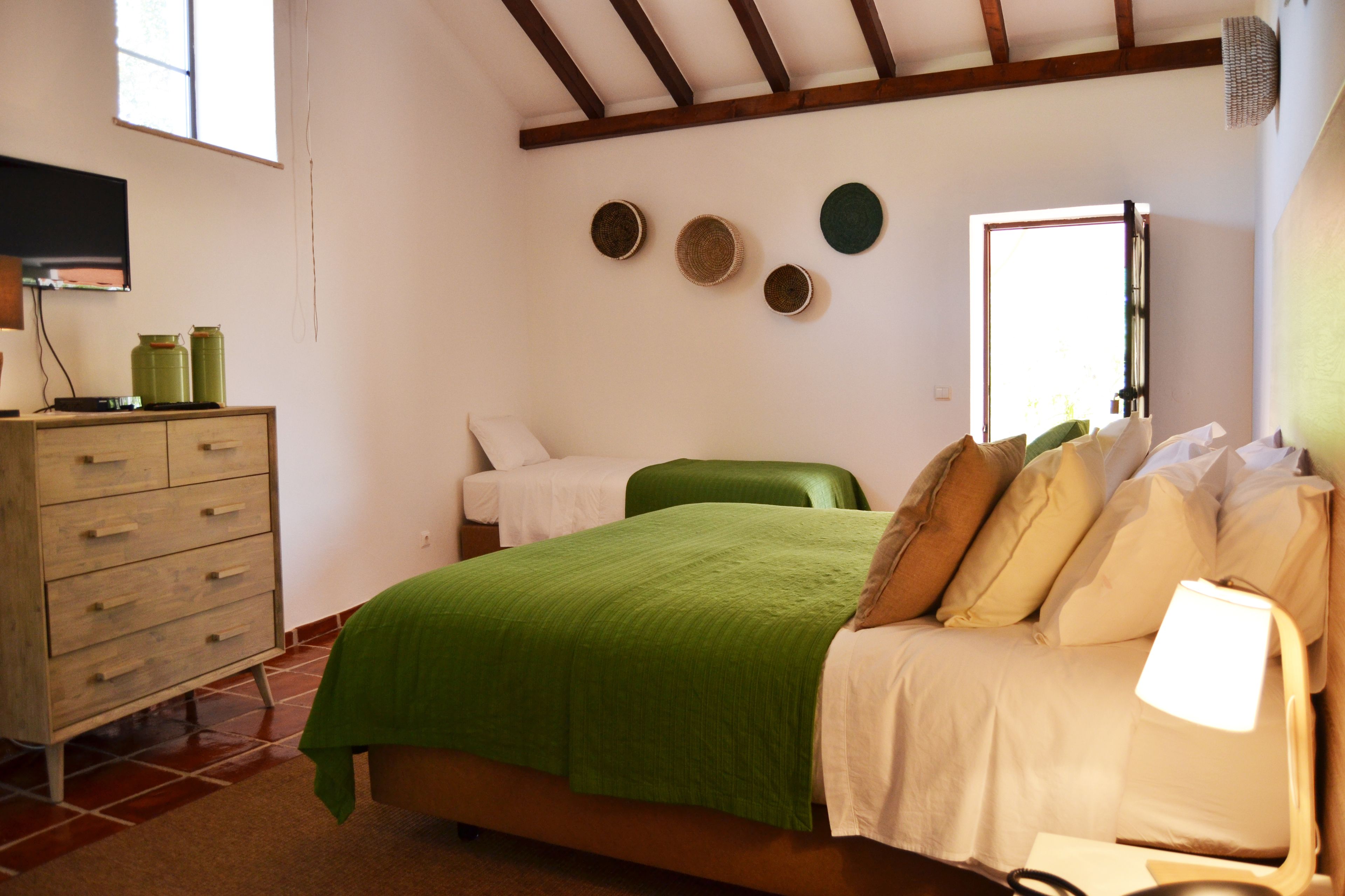 Een slaapkamer met een bed, een dressoir, een televisie en een raam.