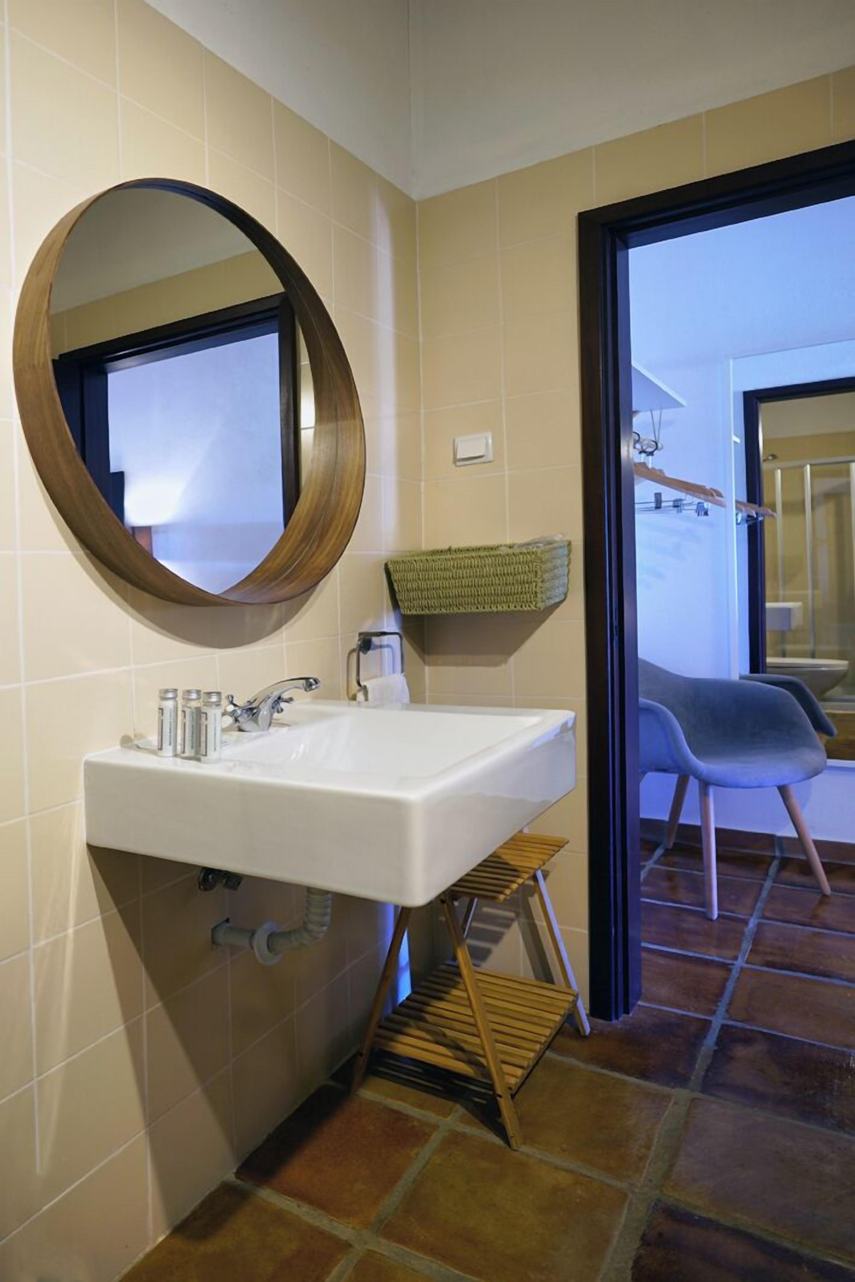 Ein Badezimmer mit einem weißen Waschbecken, einem spiegelnden Wandbild mit Holzrahmen und einem Korbwäscheschrank an der Wand.