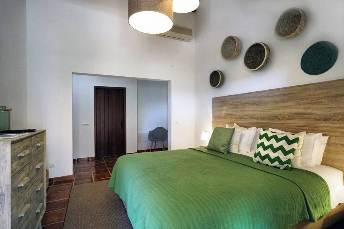 A bedroom with a green bedspread, a wooden headboard, and a wall-mounted circular decoration.