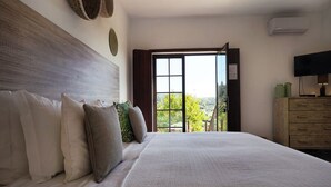 A bedroom with a large bed, a wooden headboard, a television, and a view of the outdoors through a window. - Vale Fuzeiros Nature Guest House (Silves)