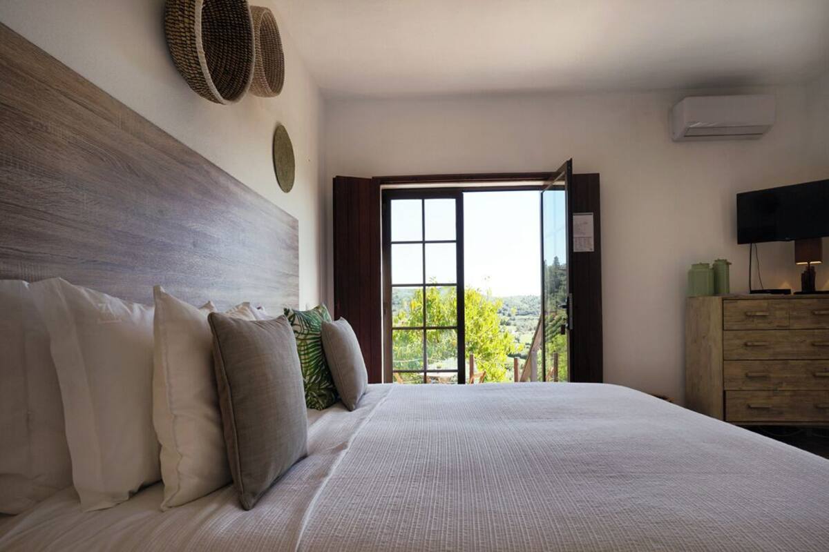 A bedroom with a large bed, a wooden headboard, a television, and a view of the outdoors through a window.
