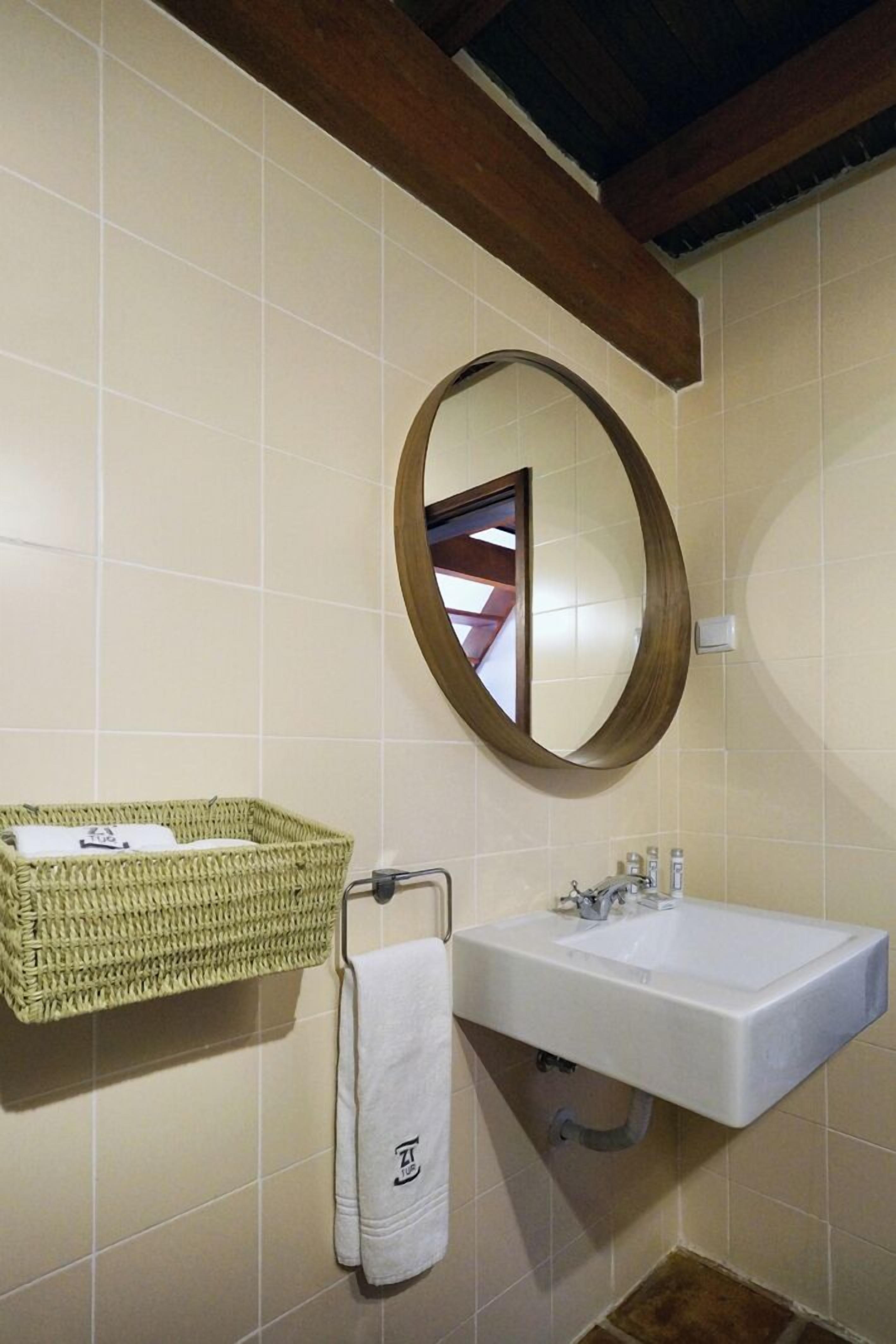 Un baño con lavamanos blanco, un espejo con marco de madera, una cesta tejida y un perchero para toallas.