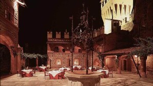 An outdoor dining area with tables and chairs, a central fountain, and a brick building in the background. - Castello di Pavone (Pavone Canavese)