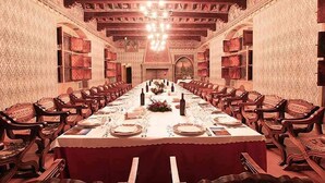 A long dining table set for a meal in a room with patterned walls and wooden chairs. - Castello di Pavone (Pavone Canavese)