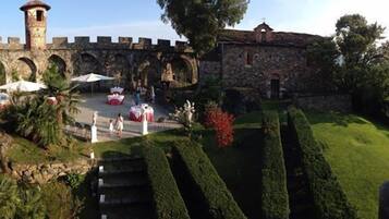 A courtyard with stone walls, a tower, and neatly trimmed hedges.