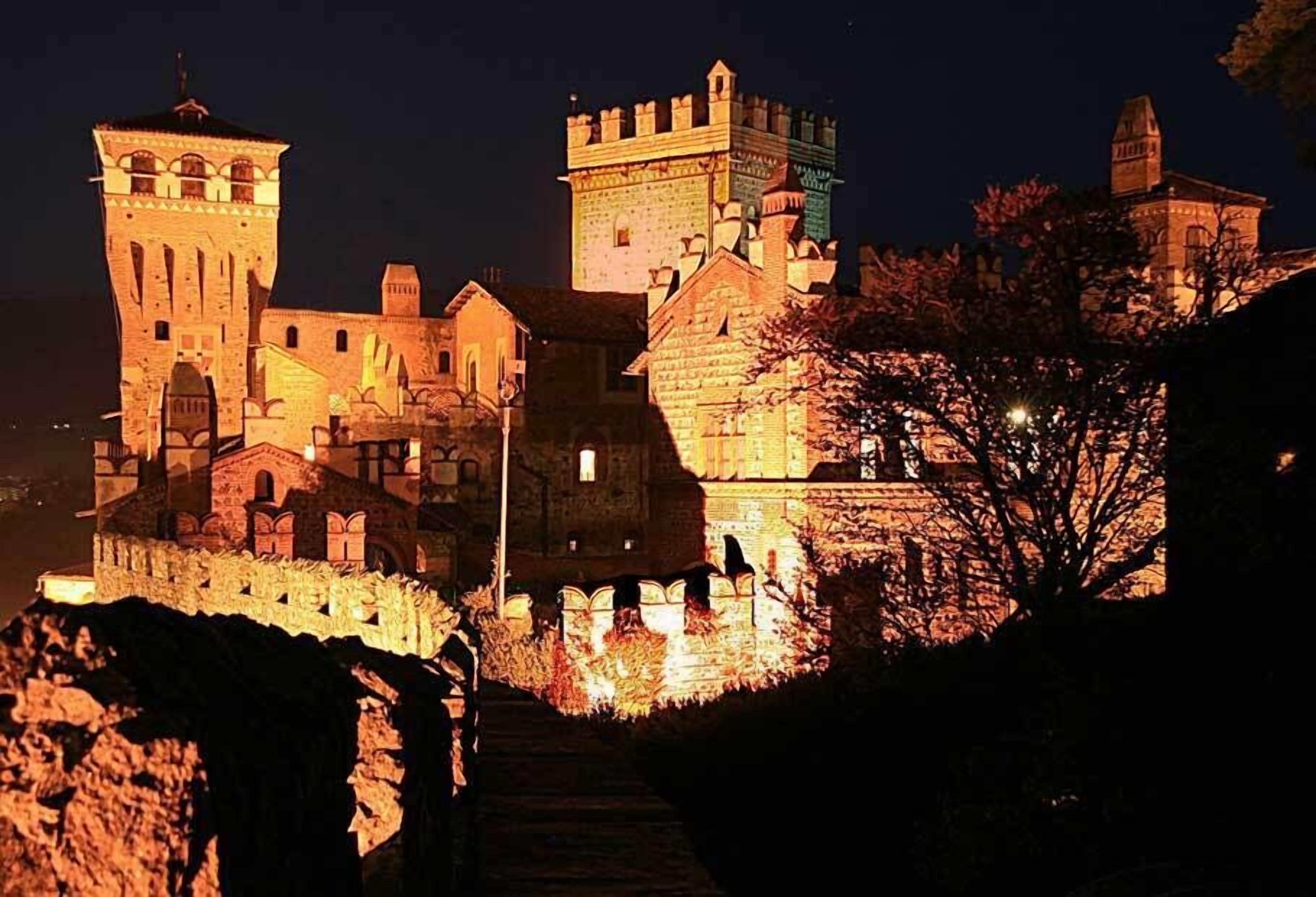 Un castillo histórico con múltiples torres y un muro fortificado, iluminado durante la noche.
