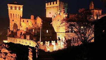 Un castillo histórico con múltiples torres y un muro fortificado, iluminado durante la noche.
