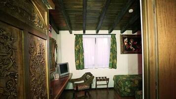 Una habitación con techo de madera, un televisor sobre un mueble de madera, un sofá verde y una pequeña mesa con una silla.