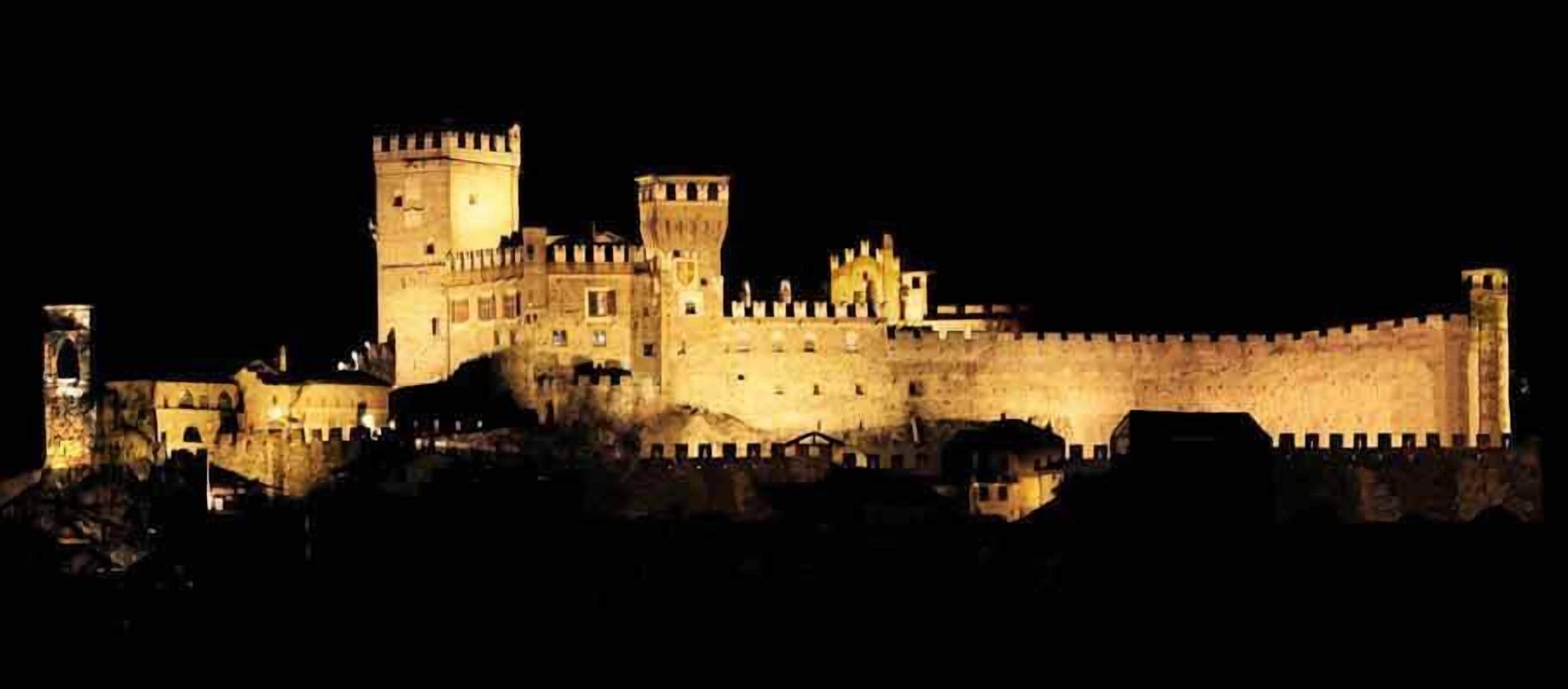 Una gran estructura iluminada que se asemeja a un castillo, con múltiples torres y un muro fortificado.