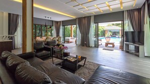 Un salon moderne avec un canapé, une table basse et un téléviseur. On y trouve également un coin repas avec des chaises et une table. La pièce est dotée de grandes fenêtres et offre une vue sur une piscine.
