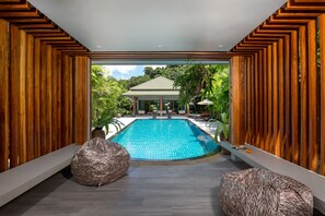 A modern pool area with wooden paneling, a clear view of a house, and two bean bags. - Karon Beach Pool Villa (Karon)