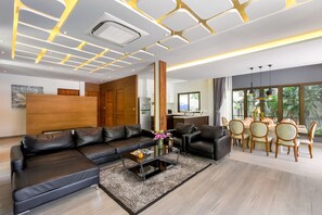 A modern living room with a sectional sofa, a dining area with a wooden table and chairs, and a kitchen in the background. - Karon Beach Pool Villa (Karon)