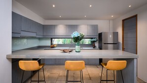 Une cuisine moderne avec des meubles gris, un grand îlot central, deux tabourets de bar jaunes et un réfrigérateur en acier inoxydable.
