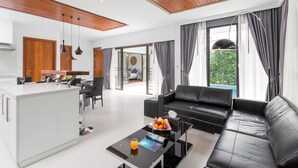 Un salon moderne avec un canapé en cuir noir, une table basse en verre et un coin repas comprenant un îlot blanc et des éléments décoratifs en bois.