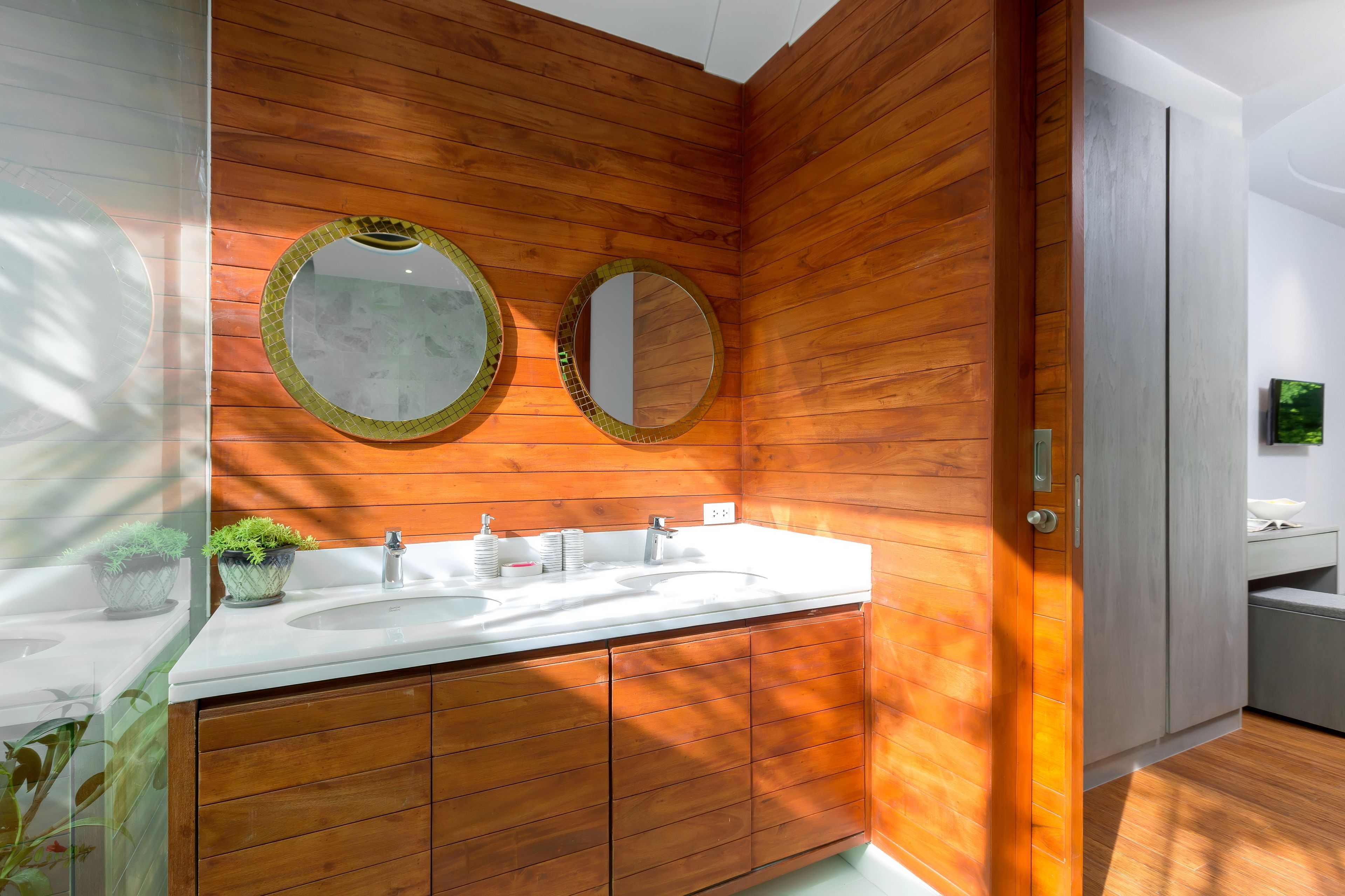 Een badkamer met houten lambrisering, twee wasbakken en twee ronde spiegels.