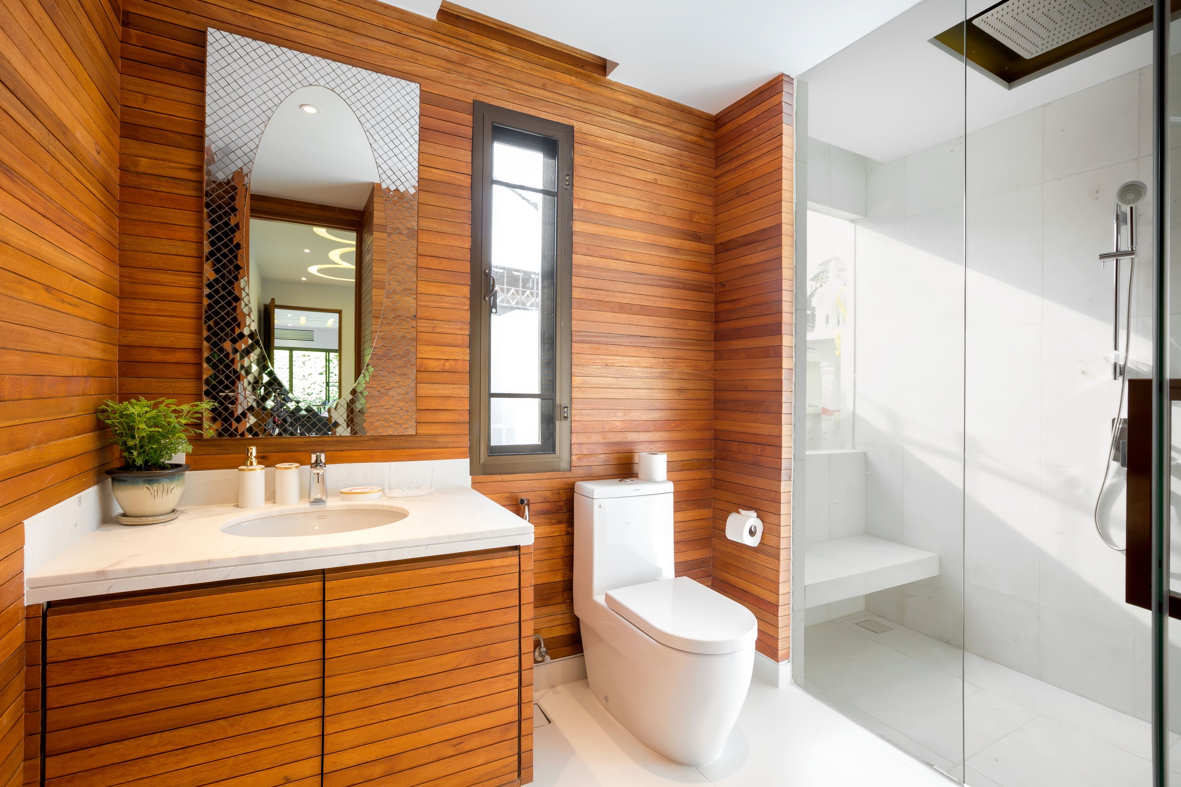 Un baño moderno con paneles de madera, un lavamanos blanco, un inodoro y un box de ducha de vidrio.