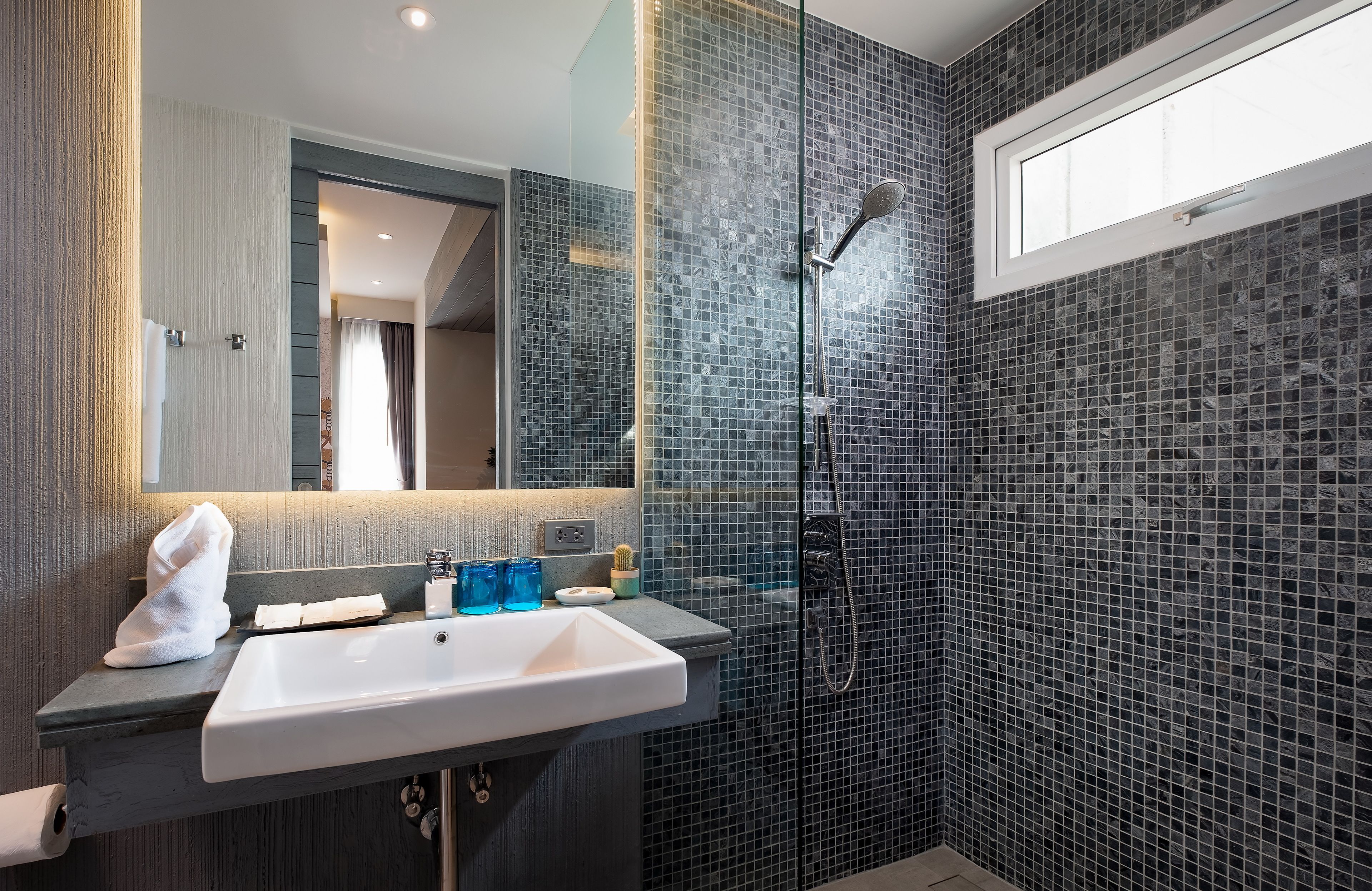 Une salle de bain moderne avec un grand miroir, un lavabo blanc et un espace douche doté d’une porte en verre.