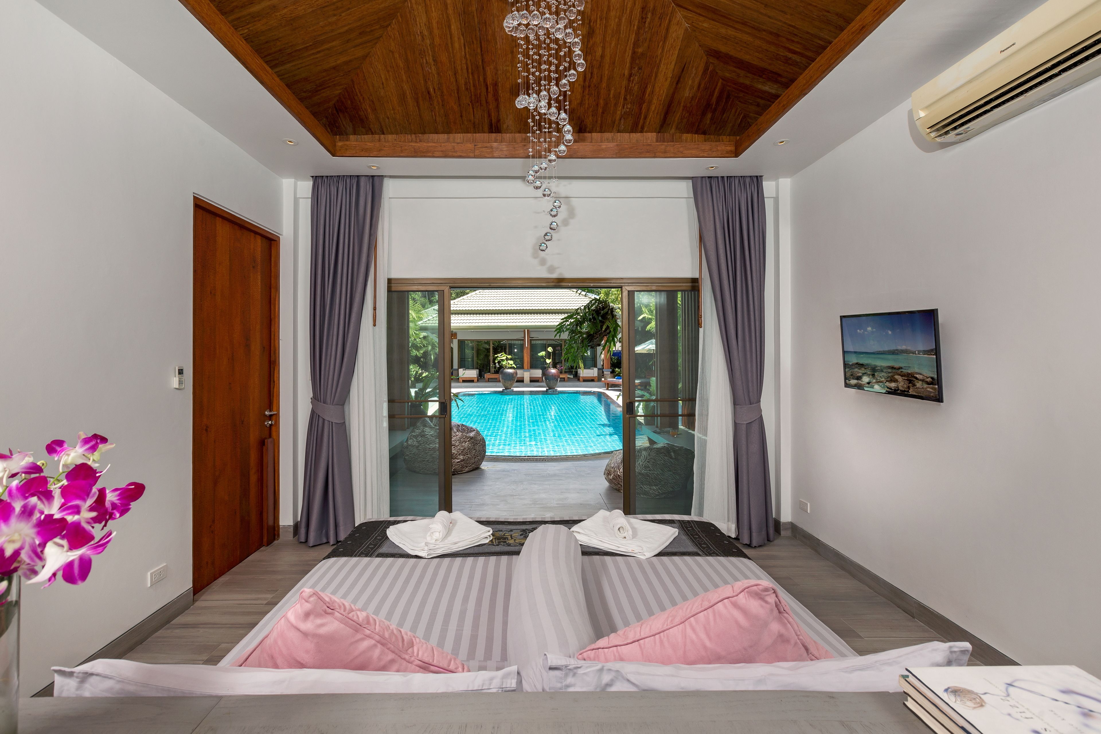 A hotel room with a bed, a view of an outdoor swimming pool, and a ceiling with wooden beams.