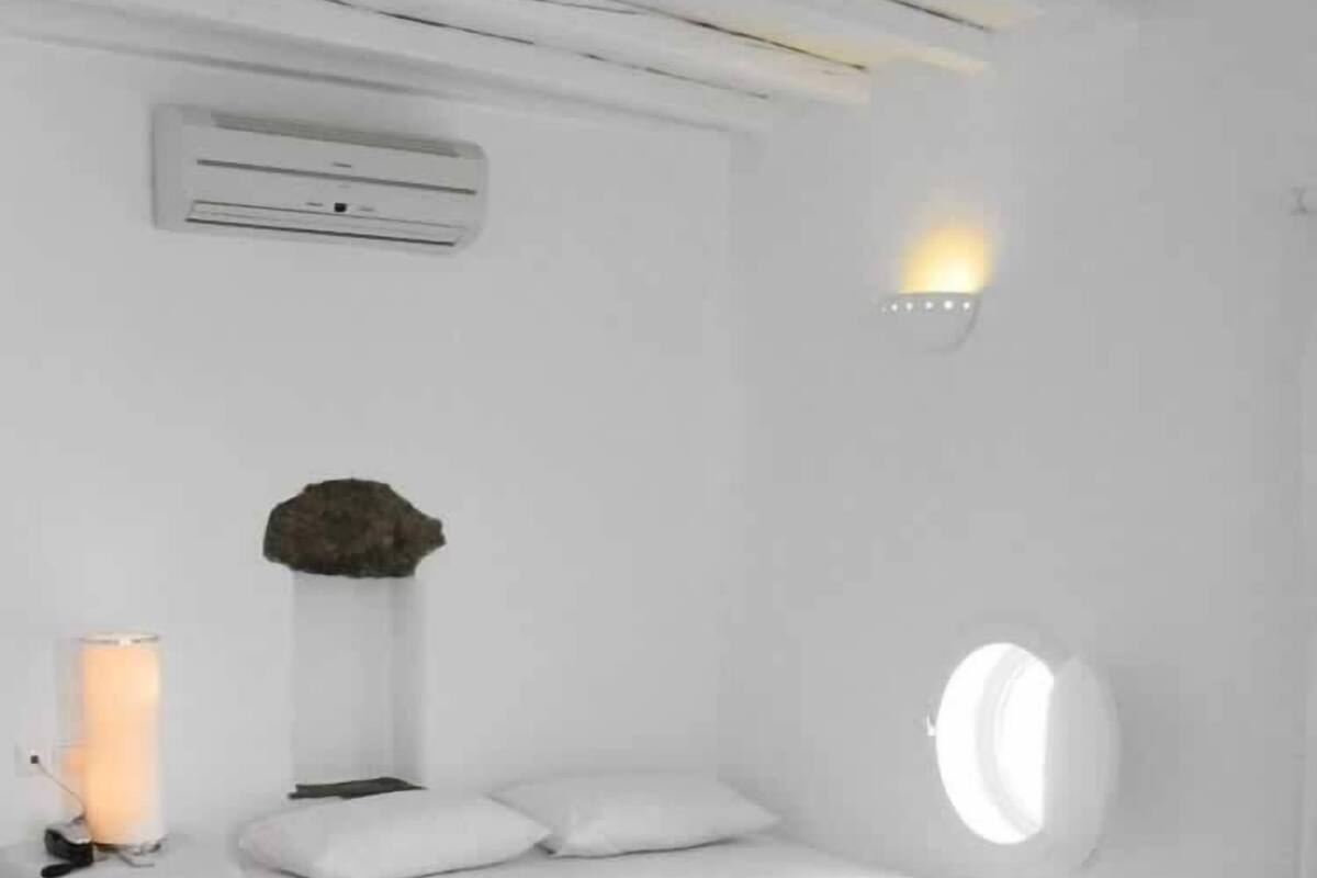 A modern bedroom with a curved bed, a bedside table, a lamp, and a wall-mounted air conditioner.