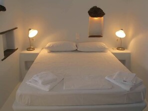 A neatly made bed with white linens and two bedside lamps. - Vega Apartments (Tinos)