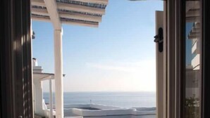 A doorway leading to a stone patio with outdoor seating and a view of the sea. - Vega Apartments (Tinos)